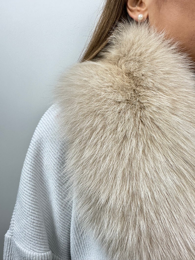 May include: A light beige fur collar with a soft, fluffy texture. The collar is made of real fur and is perfect for adding a touch of luxury to any outfit.