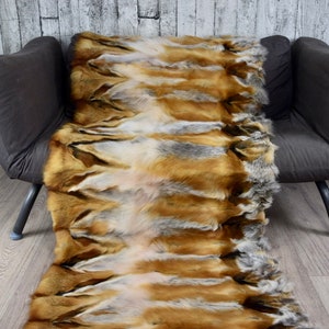 May include: A long, rectangular fur throw made from fox pelts. The fur is a mix of brown, grey, and white, and the pelts are sewn together in a striped pattern.