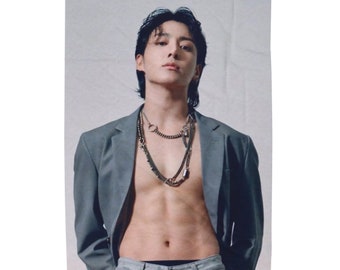 May include: A man with dark hair wearing a gray blazer with a silver chain necklace. He is shirtless and has a toned physique.