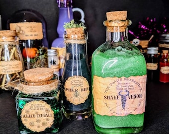 Può includere: Una collezione di bottiglie da farmacia con tappi di sughero. Le bottiglie contengono liquidi verdi e neri, con etichette che recitano "Pickled Eyeball", "Spider Bite" e "Snake Venom". Le bottiglie sono disposte su una superficie scura.