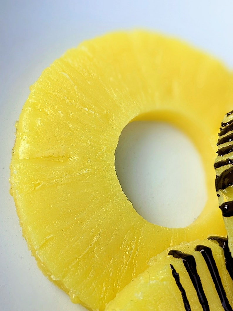 May include: A close-up of a yellow pineapple ring with a hole in the center. The ring is on a white surface.