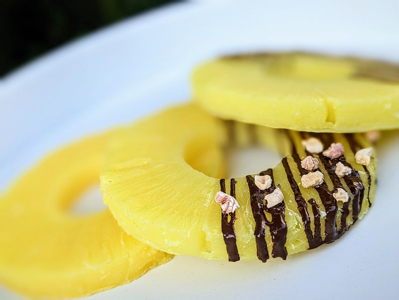 May include: Three pineapple rings on a white plate. The top ring is decorated with chocolate stripes and pink sprinkles.