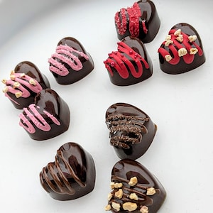 Pode incluir: Conjunto de chocolates em forma de coração decorados com gotas cor-de-rosa, vermelhas e castanhas, granulado e nozes.