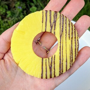 May include: A pineapple ring with chocolate drizzled on top. The ring is held in a hand, with the chocolate side facing the camera.