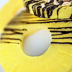May include: Close-up of a pineapple ring with a chocolate drizzle. The pineapple is yellow and the chocolate is dark brown.