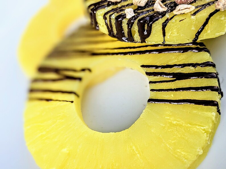 May include: Close-up of a pineapple ring with a chocolate drizzle. The pineapple is yellow and the chocolate is dark brown.