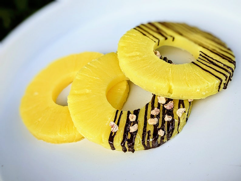 May include: Three pineapple rings on a white plate. Two of the rings are plain, while the top ring has chocolate stripes and sprinkles.