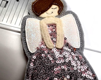 Puede incluir: Adorno de ángel de fieltro hecho a mano con cuerpo gris, cabello castaño y halo dorado. El vestido del ángel está cubierto de lentejuelas rosas y tiene alas blancas brillantes. Se adjunta una cuerda dorada para colgar.