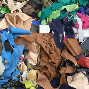 Könnte beinhalten: Ein großer Haufen bunter Lederreste in verschiedenen Brauntönen, Blau, Grün, Rosa und Weiß. Die Reste sind in einem zufälligen Muster angeordnet und scheinen bereit zum Recycling oder zur Wiederverwendung zu sein.