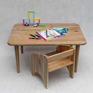 May include: A light-colored wooden children's table with rounded corners and four legs. A matching small chair is positioned in front of the table. Colorful toys, markers, and books are on the table, suggesting a play or study area.