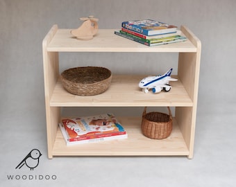 May include: A light wood bookshelf with two shelves. The top shelf has a wooden toy airplane, a stack of books, and a woven basket. The bottom shelf has a stack of children's books and a woven basket.