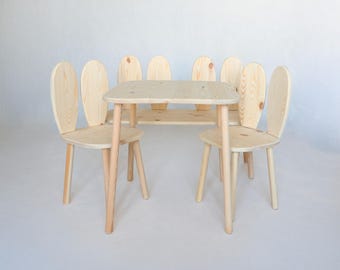May include: A light-colored wooden table and two matching chairs, each featuring a backrest shaped like a pair of tall, rounded rabbit ears. The furniture set is constructed from natural pine wood with a visible grain pattern and smooth finish.
