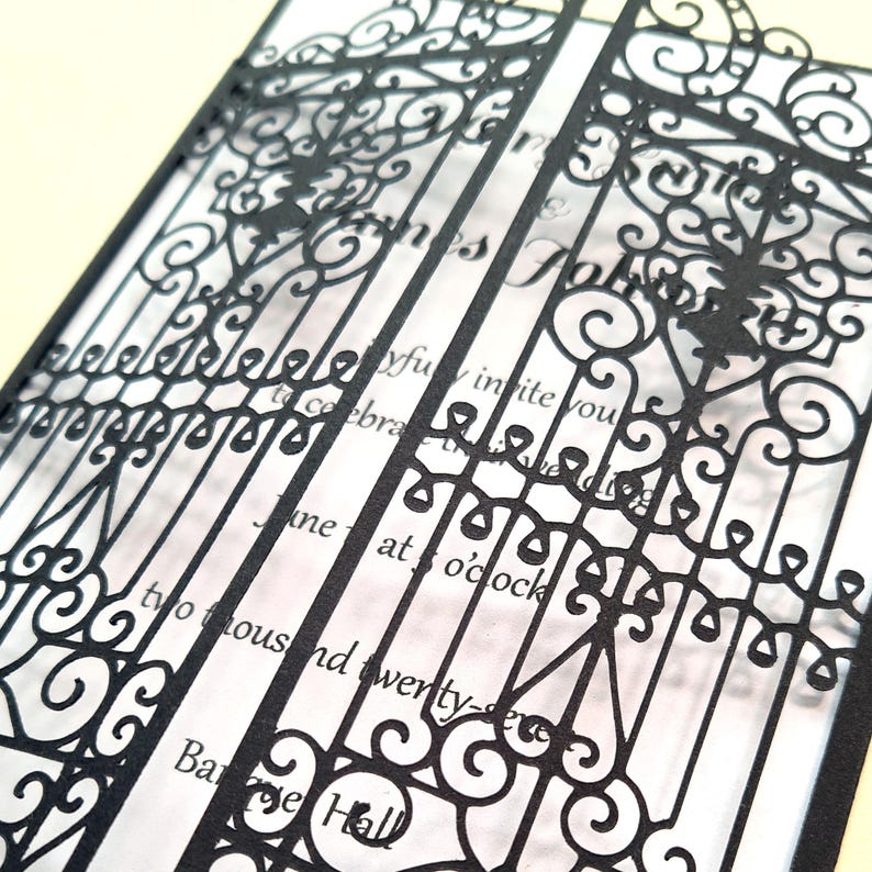 May include: A wedding invitation featuring a black laser-cut paper overlay with an intricate gate design. The overlay sits atop a white card with black printed text that reads, "joyfully invite you to celebrate the wedding," "at 5 o'clock," and "two thousand twenty-seven."