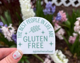 以下が含まれることがあります： 「THE BEST PEOPLE IN LIFE ARE GLUTEN FREE」の文字とInstagramのユーザー名@glutenfreeisallaeatが書かれた、薄い緑色のデザインの白いステッカー。ステッカーは花の背景の前に保持されています。