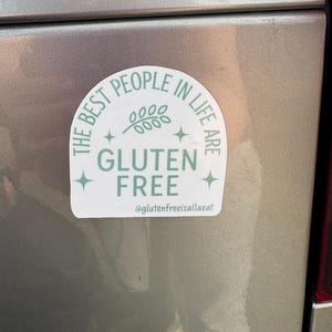 Puede incluir: Una pegatina blanca y verde claro con el texto "THE BEST PEOPLE IN LIFE ARE GLUTEN FREE" en un dise&ntilde;o circular. La pegatina tambi&eacute;n incluye una ramita de hojas y el identificador de Instagram @glutenfreeisallaeat.