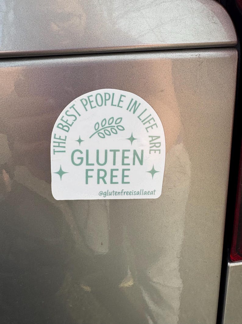 Puede incluir: Una pegatina blanca y verde claro con el texto "THE BEST PEOPLE IN LIFE ARE GLUTEN FREE" en un dise&ntilde;o circular. La pegatina tambi&eacute;n incluye una ramita de hojas y el identificador de Instagram @glutenfreeisallaeat.
