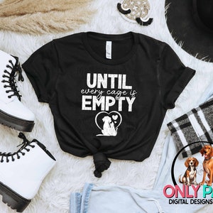 May include: Black t-shirt with white text that reads "UNTIL every cage is EMPTY" and a graphic of two dogs inside a heart.