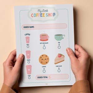 Peut inclure: Un menu coloré de café, tenu par des mains. Le menu présente des illustrations de café, de chocolat chaud, de thé, d'un biscuit et d'une part de gâteau. Le texte "My Little Coffee Shop" est en haut.