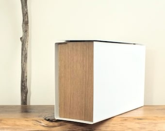 May include: A white and wood storage box with a hinged lid. The box is sitting on a wooden surface.