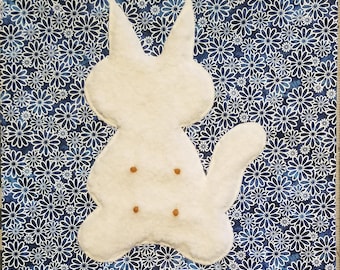 May include: A square fabric panel featuring a dark blue background with a repeating white daisy pattern. Centered on the panel is a white, plush, cat-shaped applique with two pointed ears, a curved tail, and four small, brown, circular accents.
