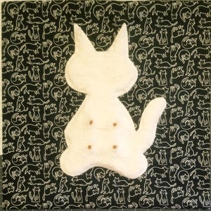 May include: A white plush cat-shaped pillow with four small brown circular accents on its front, positioned against a black fabric background featuring a repeating white line-art pattern of various sitting and walking cats.