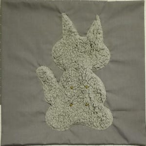 May include: A gray square pillow with a plush, light gray cat applique. The cat has button eyes and is made of a fuzzy material. The pillow is a solid gray color.