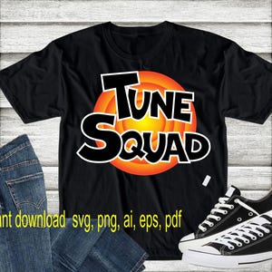 May include: Black t-shirt with a graphic of the "Looney Tunes" character, Bugs Bunny, in his signature orange and black circle. The text "Tune Squad" is written in white letters on the graphic. The t-shirt is on a wooden surface with a pair of black and white sneakers.