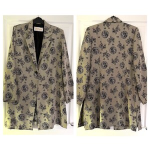 May include: A long-sleeved blazer with a grey background and a black and white pattern of stylised dragons. The blazer has a single button closure and a collar. The label on the blazer reads "Roman Originals".