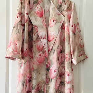 Puede incluir: Chaqueta con estampado floral con un diseño de tulipanes rosas y blancos. La chaqueta tiene cuello con solapas, mangas tres cuartos y cierre de un solo botón. La tela tiene un efecto acuarela.