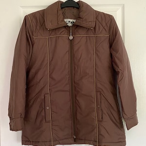 Könnte beinhalten: Eine braune gesteppte Jacke mit Reißverschluss und braunem und weißem Besatz. Die Jacke hat einen Stehkragen und zwei Taschen. Der Markenname "Land's End" ist auf der Jacke sichtbar.