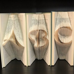 May include: Three open books with folded pages forming the numbers "369". The pages are folded to create the shapes, with the text of the book visible. The books have light green covers and are set against a dark background.