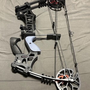 May include: A black compound bow with a light blue grip and red accents. The bow features a complex system of pulleys, cables, and a sight for aiming. The bow is designed for precision and power in archery.