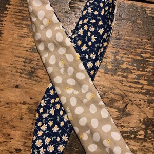 May include: A reversible fabric headband with a beige and white polka dot pattern on one side and a navy blue fabric with a white daisy print on the other side.