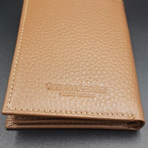 May include: A brown leather wallet with a stitched edge and the text "Genuine Leather Hand Made" embossed on the front.