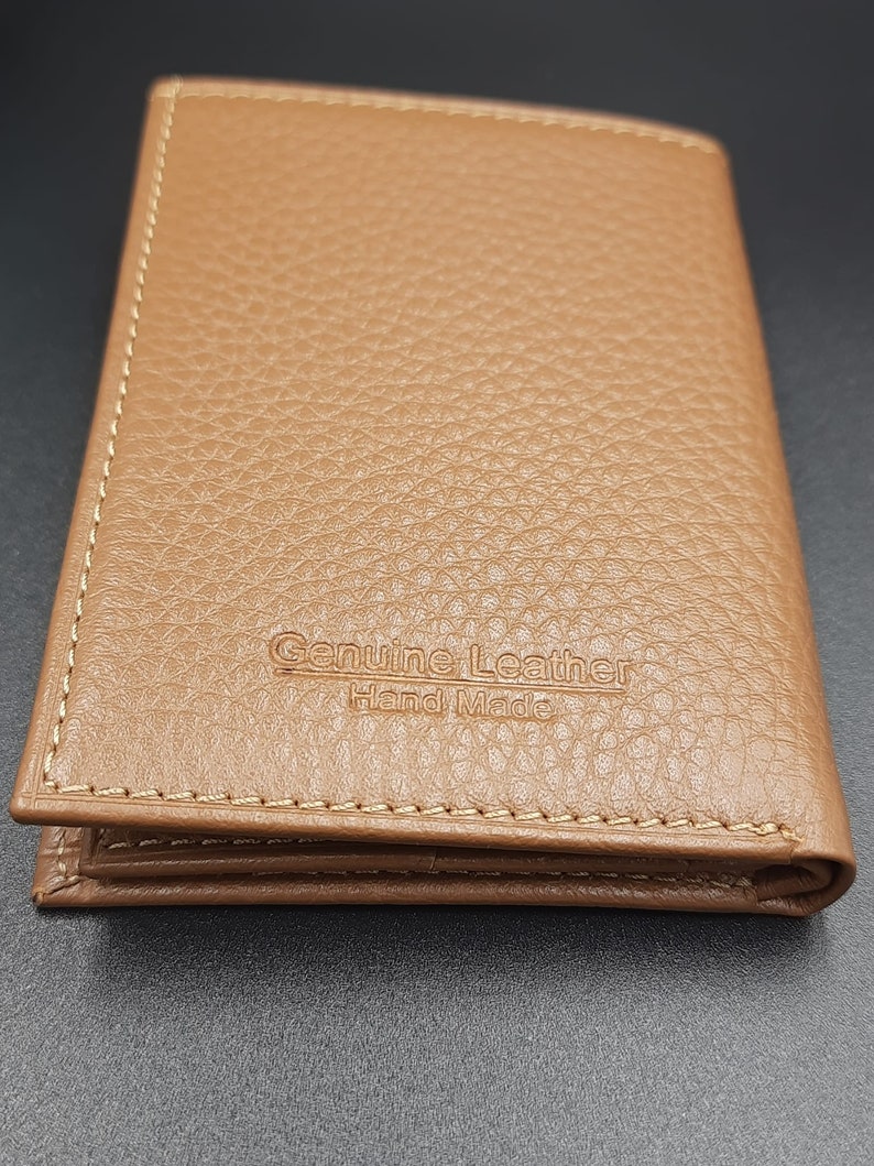 May include: A brown leather wallet with a stitched edge and the text "Genuine Leather Hand Made" embossed on the front.