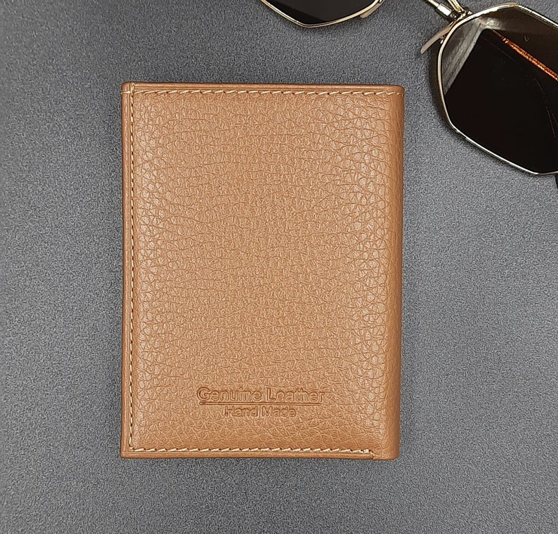 May include: A brown leather wallet with a stitched border and the text "Genuine Leather Hand Made" embossed on the front.