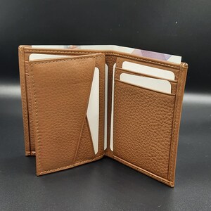 May include: A brown leather wallet with multiple card slots and a billfold. The wallet is open to show the interior.