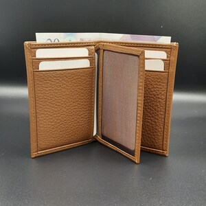 May include: A brown leather wallet with multiple card slots and a clear ID window. The wallet is open and has a billfold.