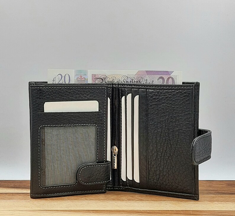 Puede incluir: Una cartera de cuero negro con m&uacute;ltiples ranuras para tarjetas y un compartimento con cremallera. La cartera est&aacute; abierta y tiene un billete de veinte libras dentro.