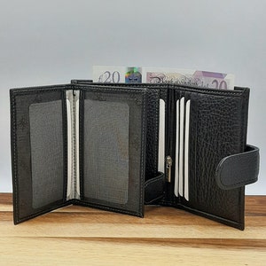 Puede incluir: Una cartera de cuero negro con m&uacute;ltiples ranuras para tarjetas y un portafolios. La cartera est&aacute; abierta y tiene un compartimento con cremallera. La cartera est&aacute; sobre una superficie de madera.