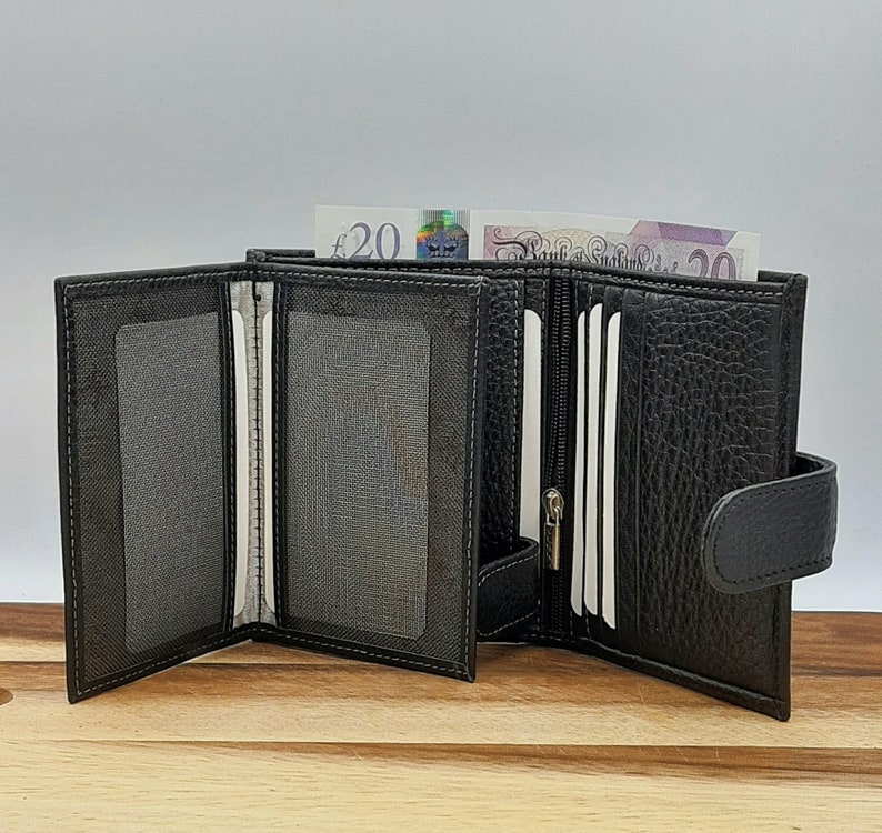 Puede incluir: Una cartera de cuero negro con m&uacute;ltiples ranuras para tarjetas y un portafolios. La cartera est&aacute; abierta y tiene un compartimento con cremallera. La cartera est&aacute; sobre una superficie de madera.