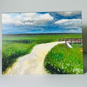 May include: A rectangular painting depicting a landscape with a light-colored dirt path winding through a vibrant green grassy field toward a wooden bridge. The horizon features a deep blue sky filled with large, textured white and gray clouds.