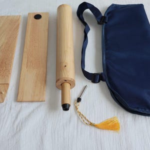 May include: A disassembled wooden massage tool set, including a long cylindrical roller, two flat wooden pieces, and a navy blue carrying case with a shoulder strap. A small metal tool with a yellow tassel is also included.