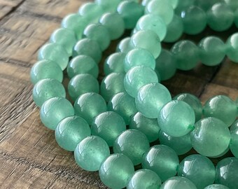 Op de afbeelding: Een streng lichtgroene jade kralen. De kralen zijn rond en glad en zijn aan elkaar geregen op een doorzichtige draad.
