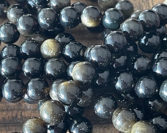 May include: A strand of black and gold gemstone beads. The beads are round and have a smooth, polished finish. The gold flecks in the beads create a shimmering effect.
