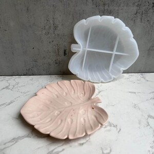 Könnte beinhalten: Zwei blattförmige Silikonformen, eine weiße und eine rosa. Die weiße Form hat vier Abschnitte, während die rosa Form ein einzelnes Stück ist.