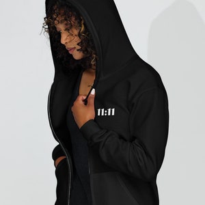May include: A black zip-up hoodie with a white "11:11" graphic on the front. The hoodie has a hood and a zipper closure.
