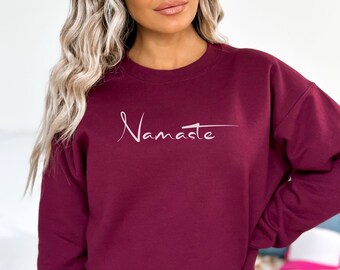 Może przedstawiać: Bordowy sweter z napisem "Namaste" napisanym białym pismem z przodu.