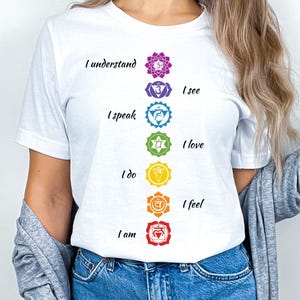 May include: White t-shirt with a vertical row of seven colorful chakra symbols and the text "I understand", "I see", "I speak", "I love", "I do", "I feel", and "I am".
