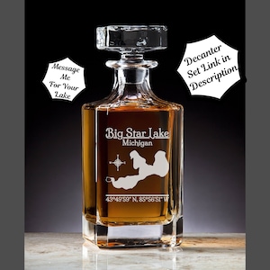 May include: A clear glass decanter with a square base and a stopper. The decanter is engraved with the words "Big Star Lake, Michigan" and the coordinates "43°49'59" N, 85°56'51" W".